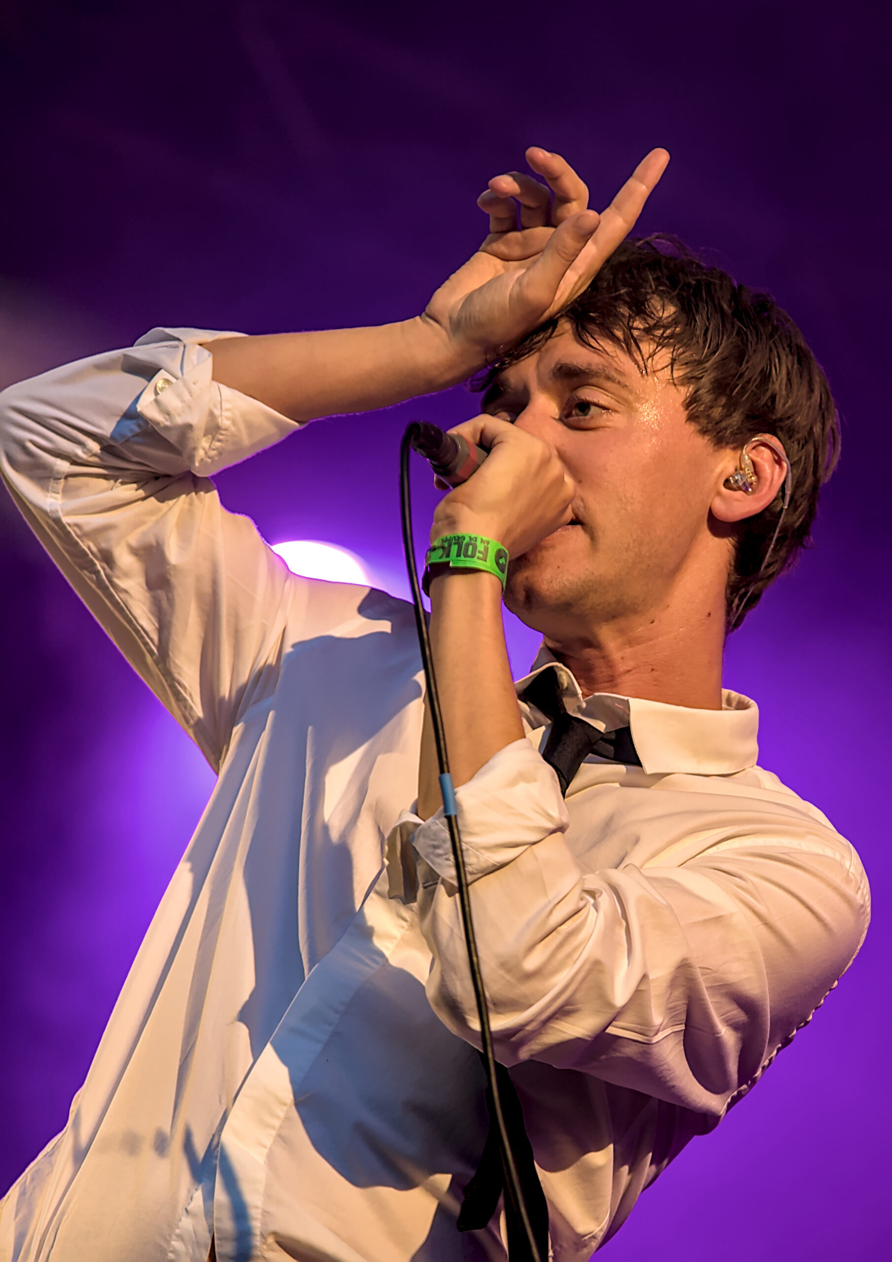 Expresieve concertfoto van een zanger in een licht overhemd op een paars uitgelicht podium tijdens een live optreden - Matt West Visuals