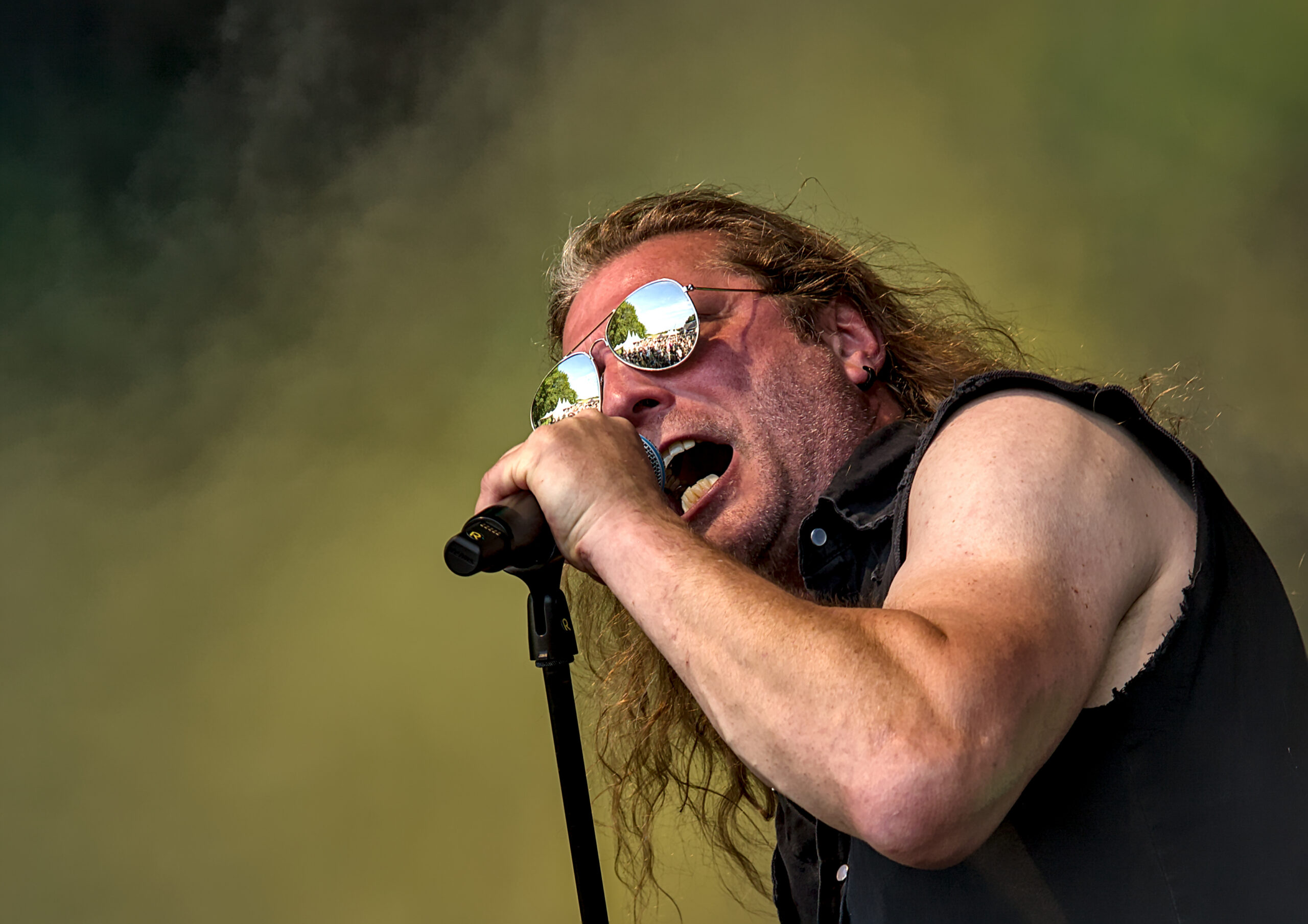 Krachtige concertfoto van een rockzanger met zonnebril die intens zingt in een microfoon tijdens een live optreden - Matt West Visuals